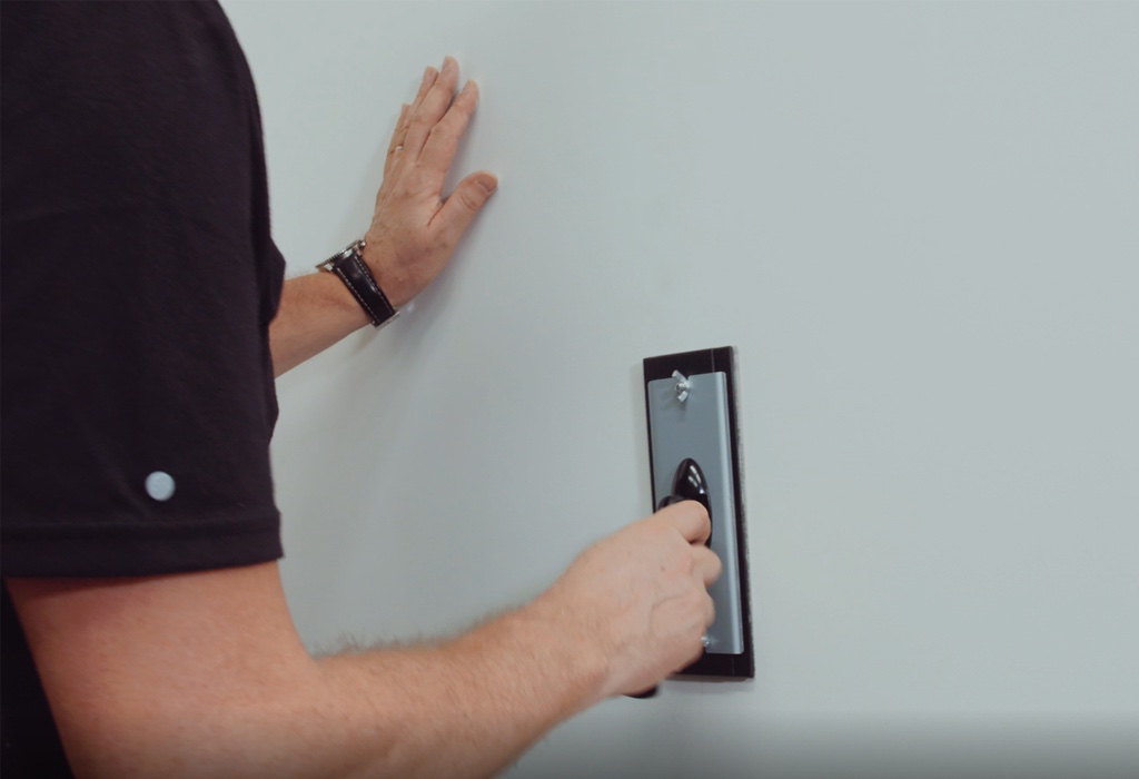 Person using a trowel on a white wall while steadying it with their other hand.