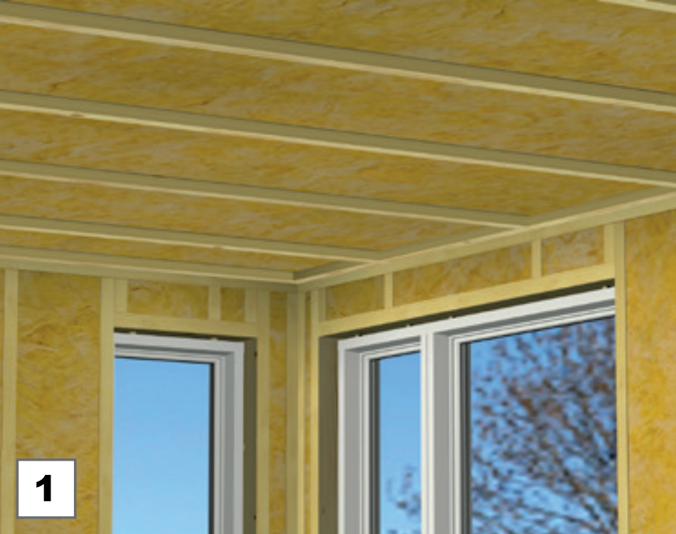 interior view of a room under construction with insulation visible in the walls and ceiling, and two large windows showing a tree outside.