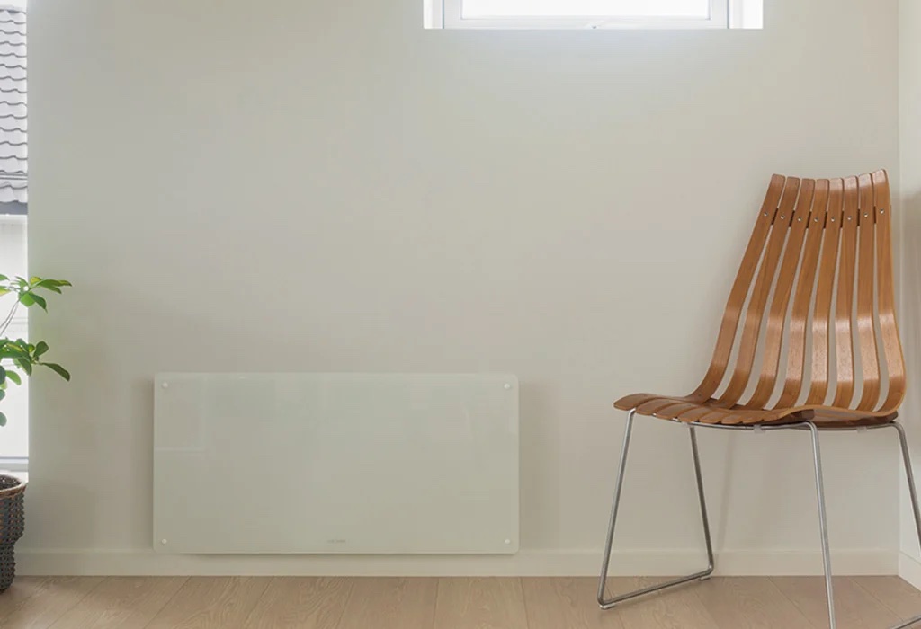 A minimalist room with a white wall-mounted heater, a wooden chair with metal legs, and a potted plant, under a small window.