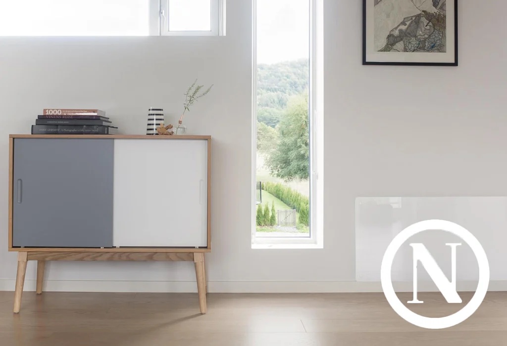 Modern living room with a wooden cabinet, books, and vase. Large window with a scenic outdoor view. White wall with framed artwork.