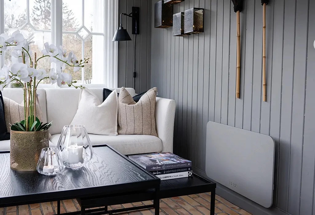 A modern living room with a white sofa, cushions, and a black coffee table. Decorative items include white orchids and candles. The walls are gray with bamboo accents.